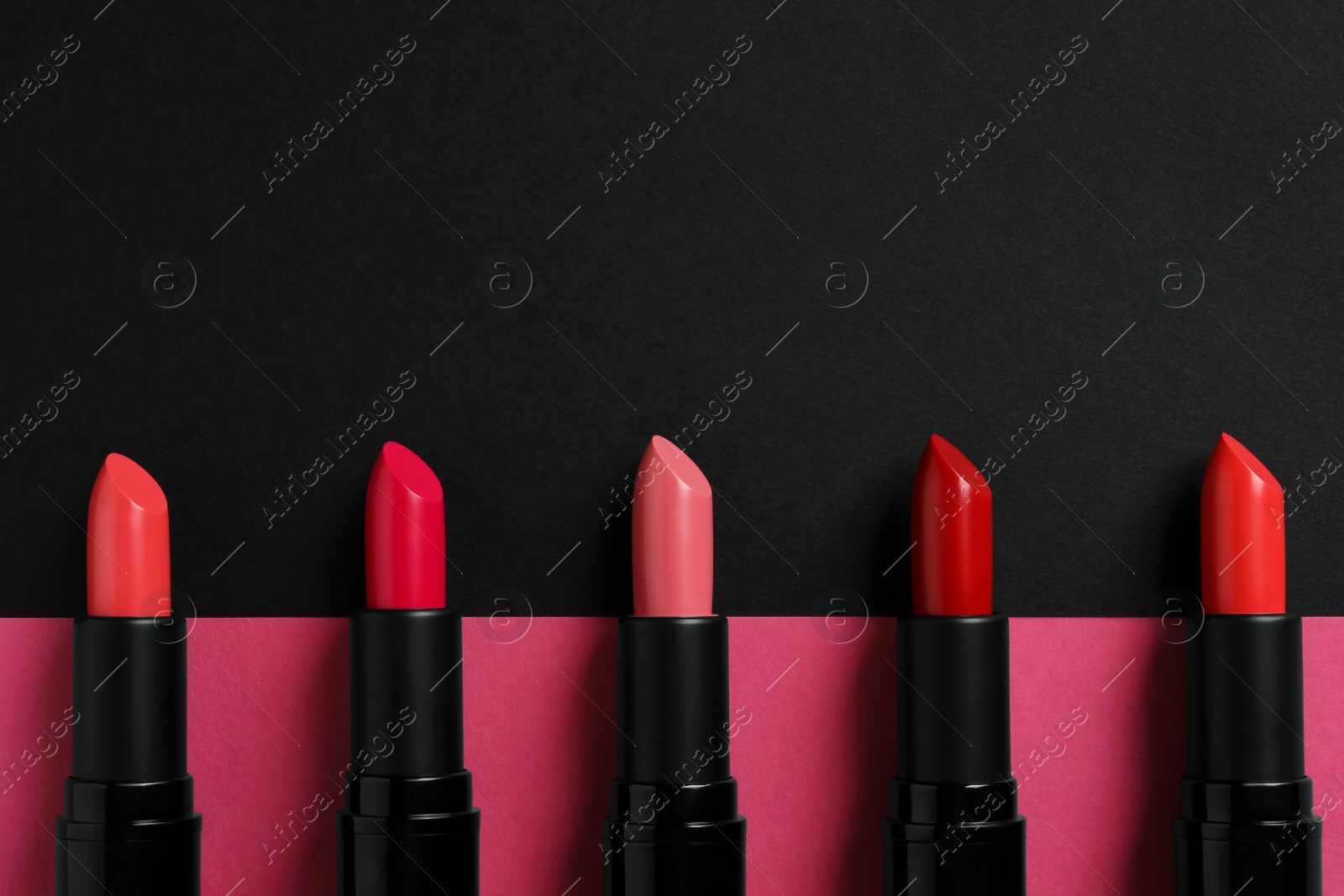 Photo of Beautiful lipsticks on black and pink background, flat lay. Space for text