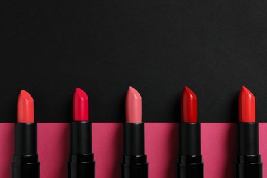 Photo of Beautiful lipsticks on black and pink background, flat lay. Space for text