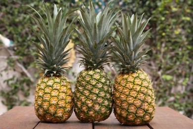 Photo of Delicious ripe pineapples on wooden table outdoors