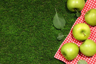 Ripe green apples with leaves and picnic blanket on grass, flat lay. Space for text