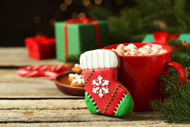 Photo of Tasty cookie in shape of Christmas stocking, cocoa with marshmallows and fir tree branch on wooden table, closeup. Space for text