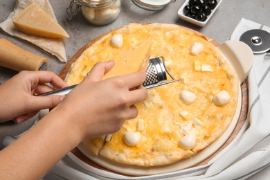 Photo of Woman grating cheese onto homemade pizza on table