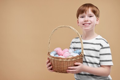 Easter celebration. Cute little boy with wicker basket full of painted eggs on dark beige background. Space for text