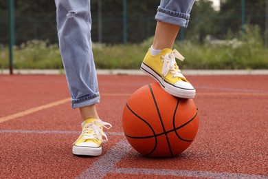 Photo of Woman with basketball ball wearing yellow classic old school sneakers on court outdoors, closeup