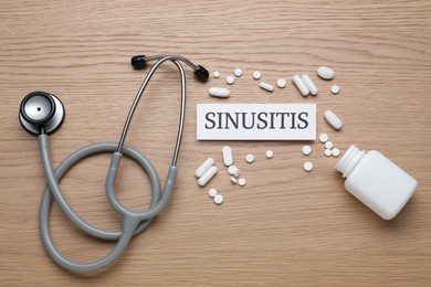 Card with word Sinusitis, stethoscope and pills on wooden table, flat lay