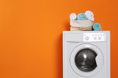 Washing machine with clean towels on orange background, space for text