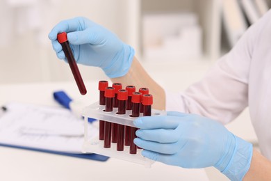 Doctor with samples of blood in test tubes at white table, closeup