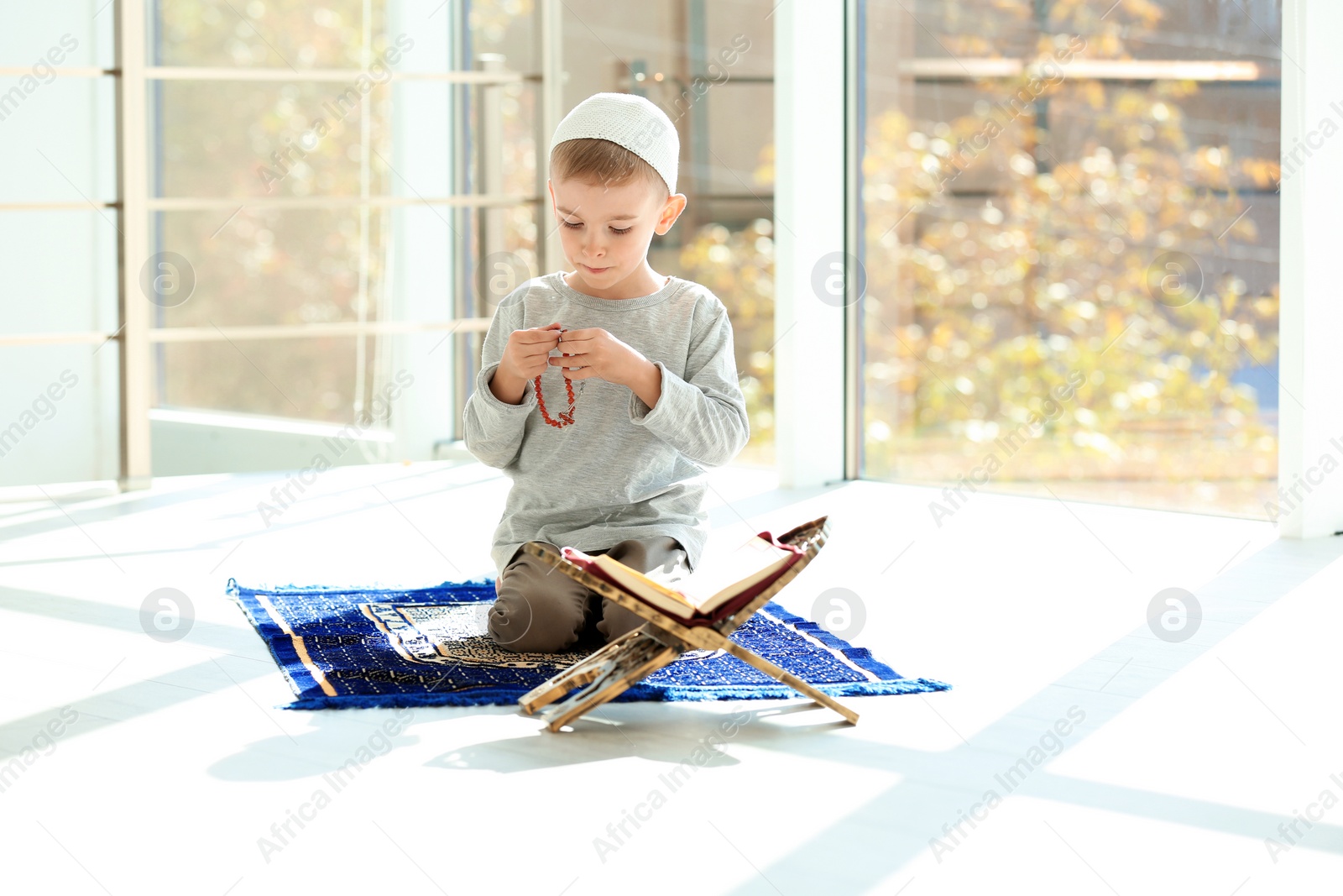 Photo of Little Muslim boy with misbaha and Koran praying on rug indoors