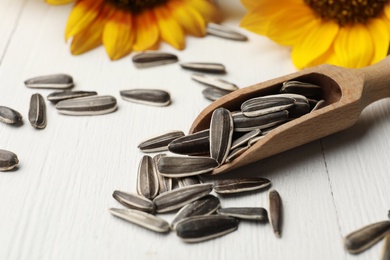 Photo of Raw sunflower seeds and scoop on white wooden table, closeup