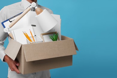 Photo of Unemployed young man with box of personal office belongings on light blue background, closeup. Space for text