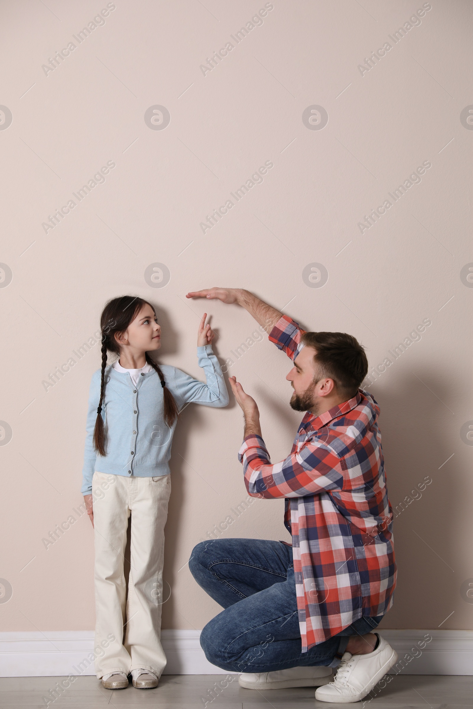 Photo of Father measuring daughter's height near beige wall indoors, space for text