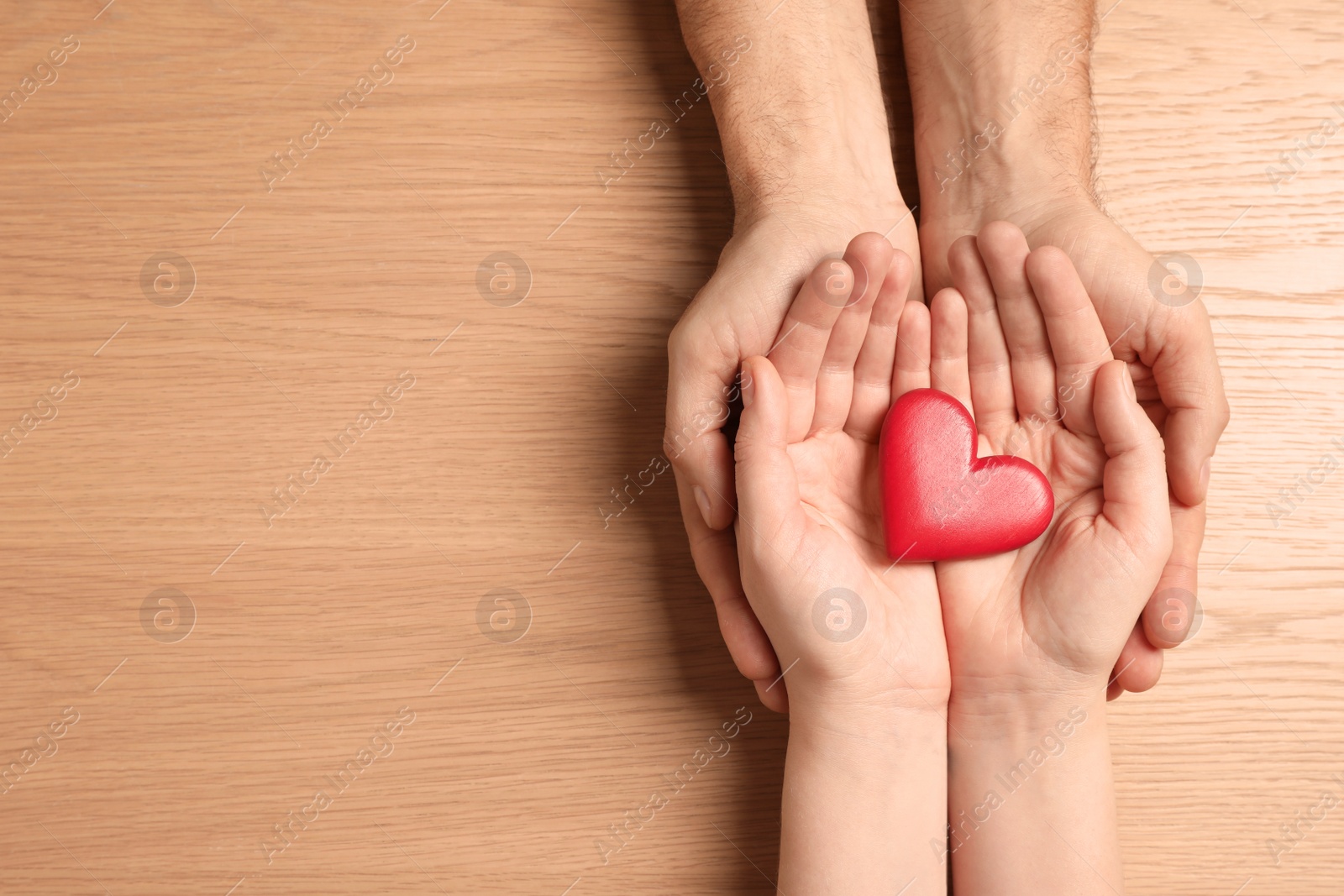 Photo of Couple holding red heart in hands at wooden table, top view. Space for text