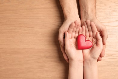 Couple holding red heart in hands at wooden table, top view. Space for text