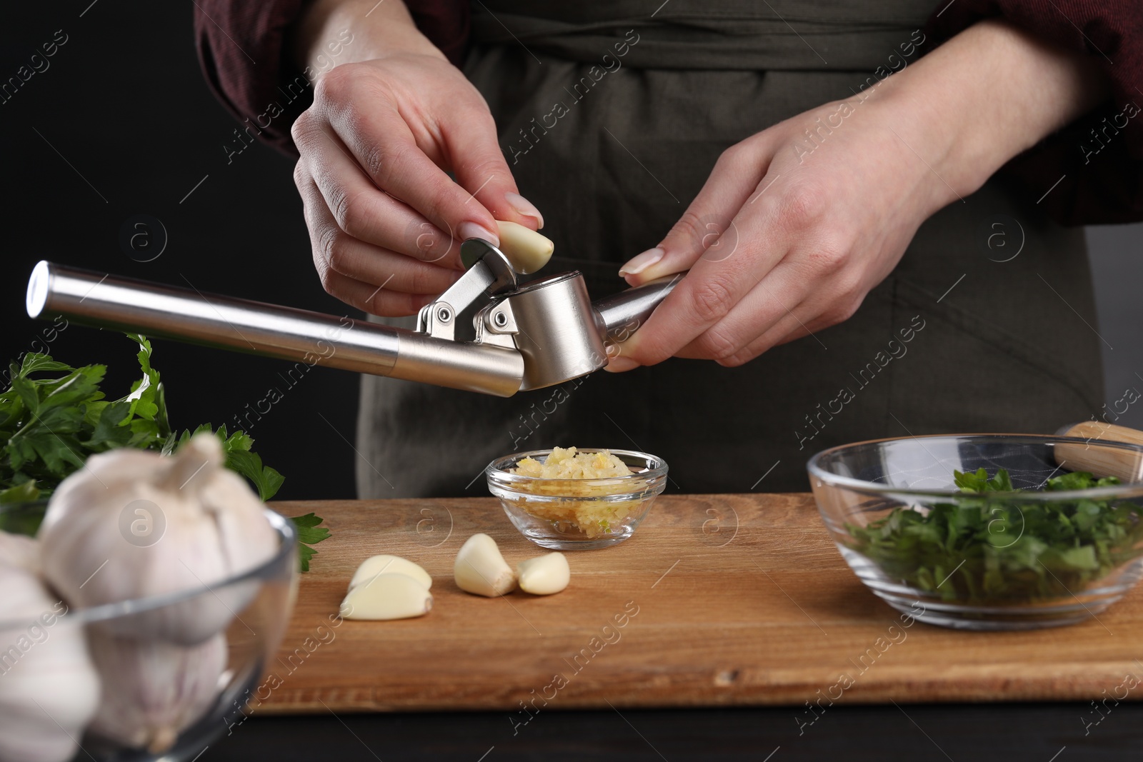 Photo of Woman squeezing garlic with press at black table, closeup