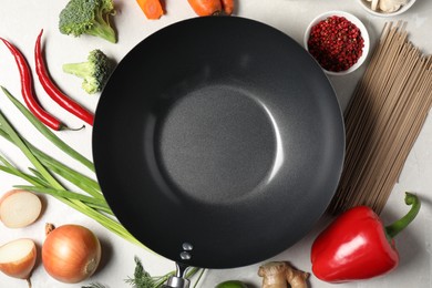 Photo of Empty iron wok surrounded by raw ingredients on light table, flat lay