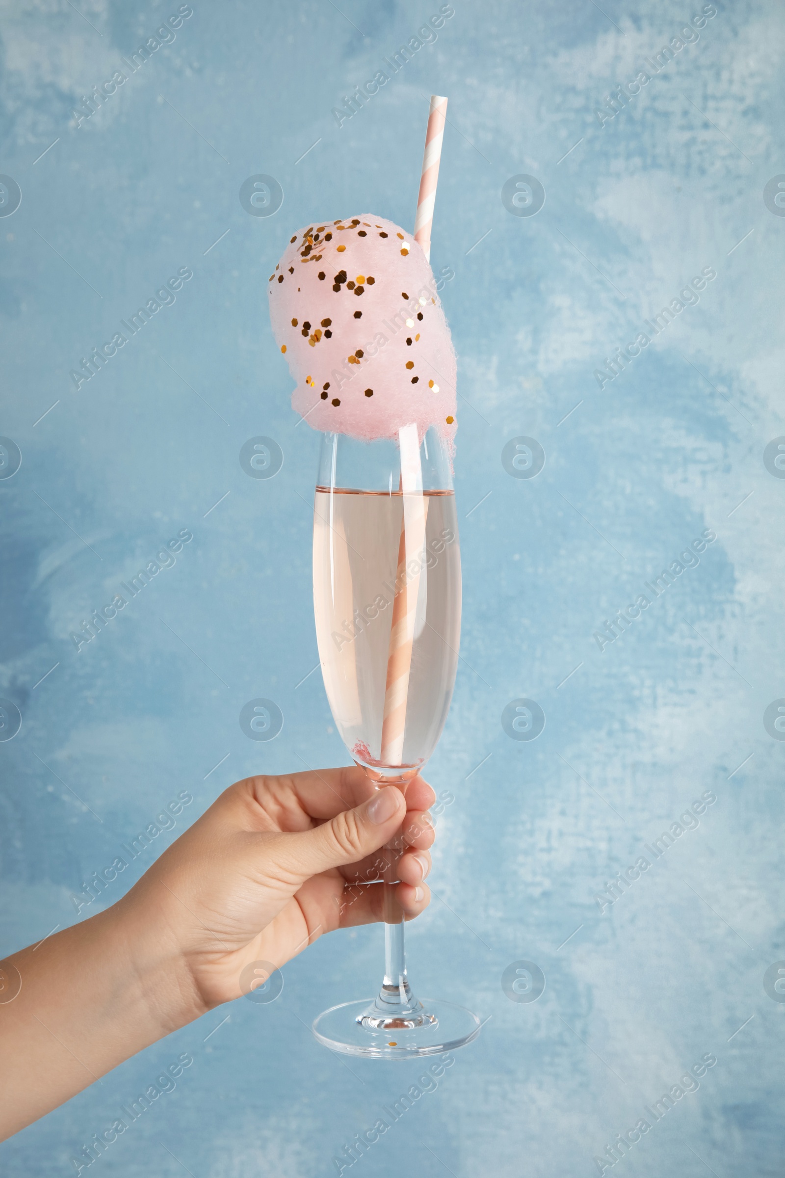 Photo of Woman holding cocktail with sweet cotton candy on light blue background, closeup view