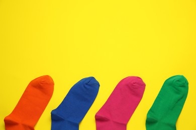 Different colorful socks on yellow background, flat lay. Space for text