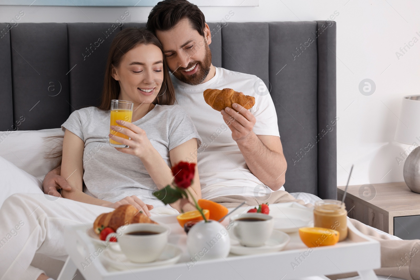 Photo of Happy couple eating tasty breakfast on bed at home