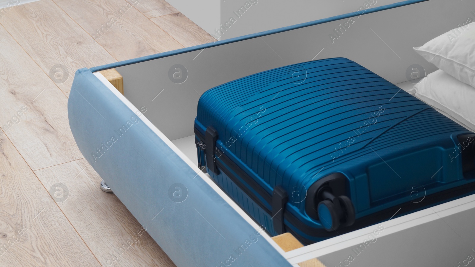 Photo of Storage drawer under bed with blue suitcase and white pillows indoors