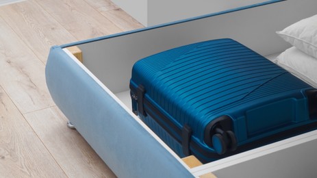 Photo of Storage drawer under bed with blue suitcase and white pillows indoors