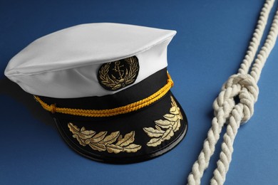 Photo of Peaked cap with accessories and rope on blue background