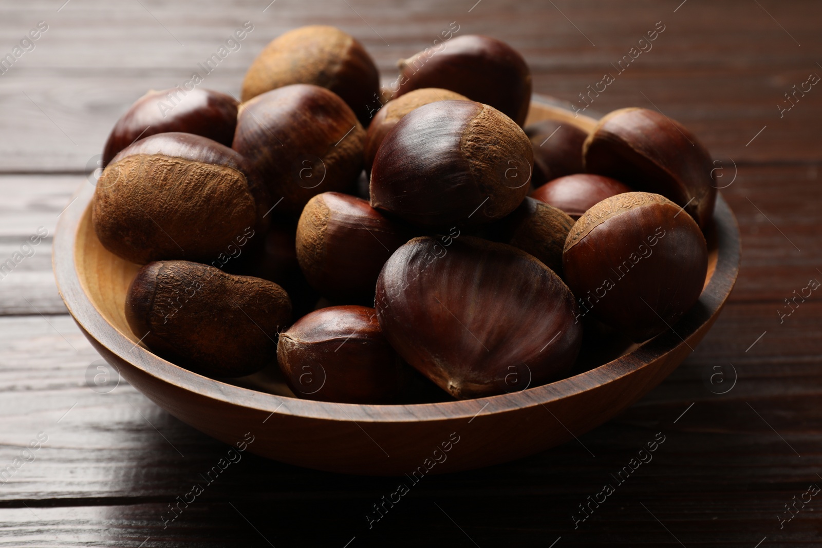 Photo of Sweet fresh edible chestnuts in bowl on wooden table, closeup