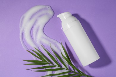 Bottle with cleansing foam and green leaves on violet background, flat lay. Cosmetic product