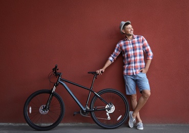 Handsome man with modern bicycle near red wall outdoors