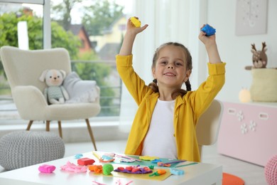 Photo of Happy girl with play dough at table in kindergarten