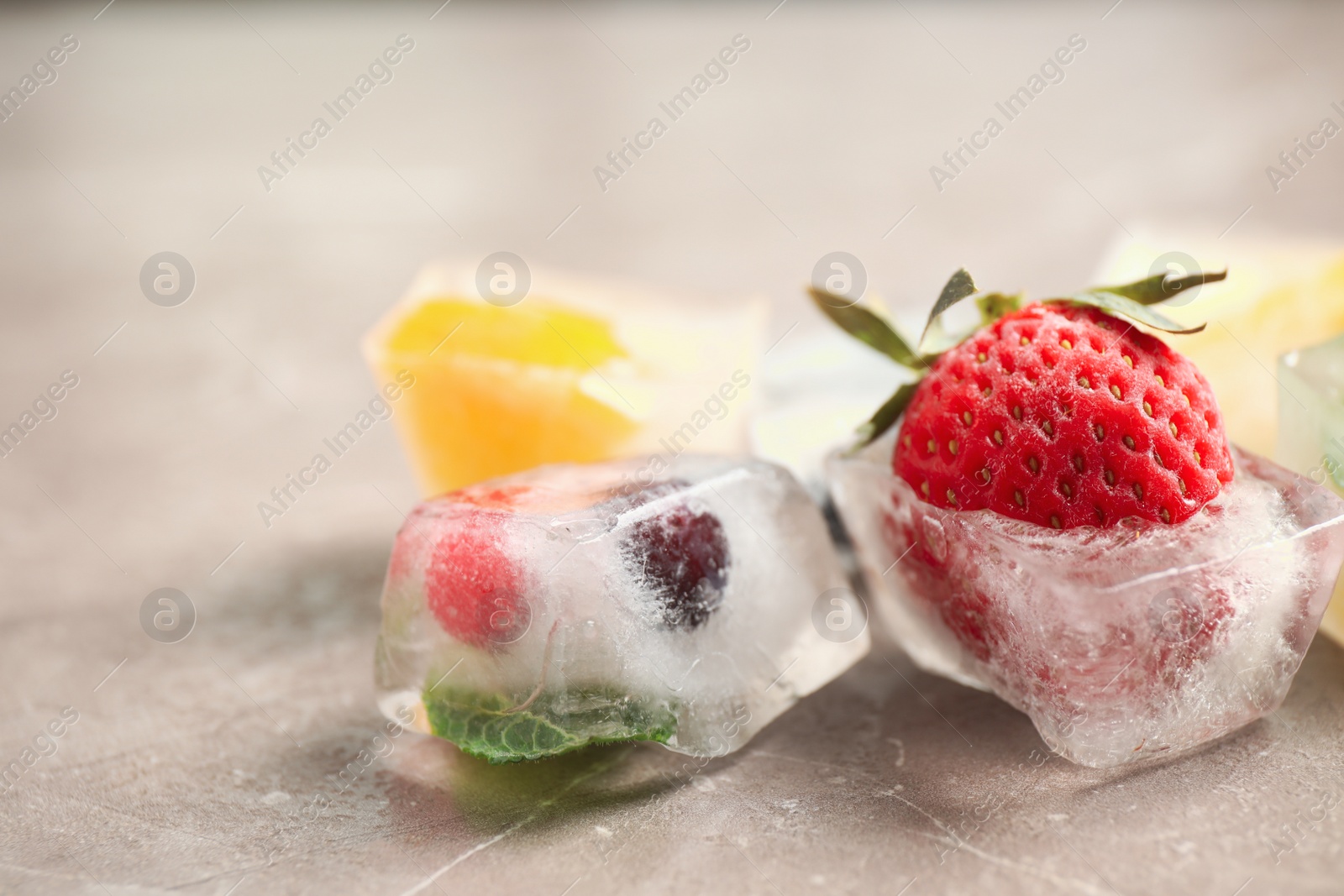 Photo of Ice cubes with different berries and mint on grey table, closeup