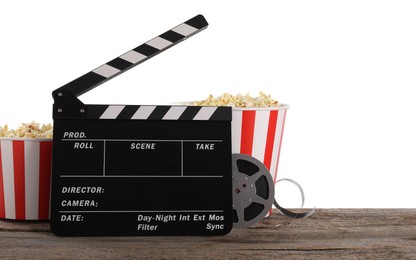 Movie clapper, buckets of tasty popcorn and film reel on wooden table against white background, space for text