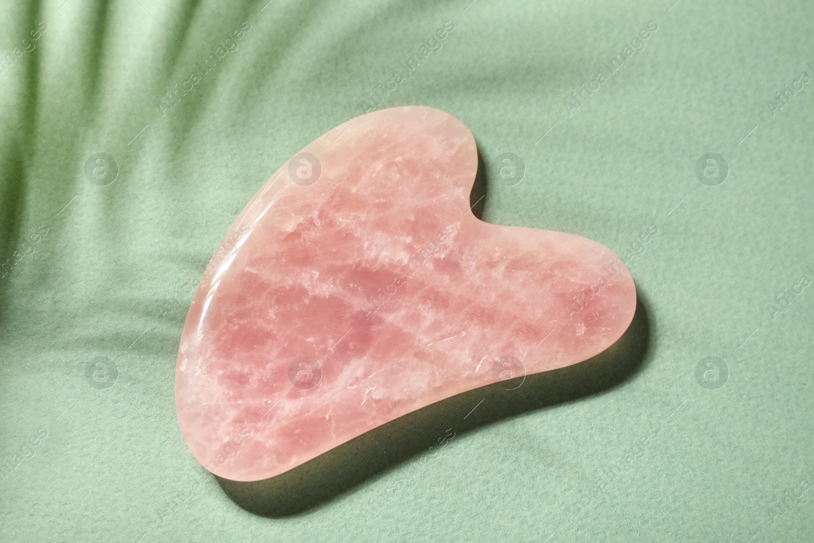 Photo of Rose quartz gua sha tool on green paper, top view