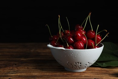 Photo of Wet red cherries in colander on wooden table, space for text