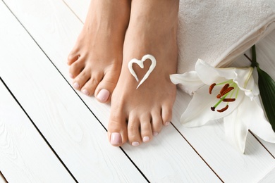 Photo of Woman with beautiful feet, cream, flower and towel on white wooden floor, closeup. Spa treatment
