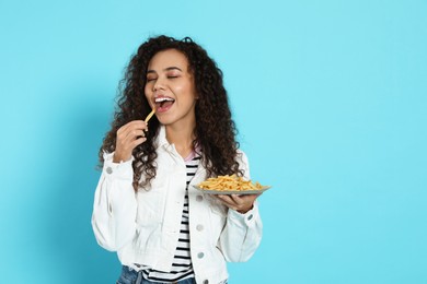 African American woman eating French fries on light blue background, space for text