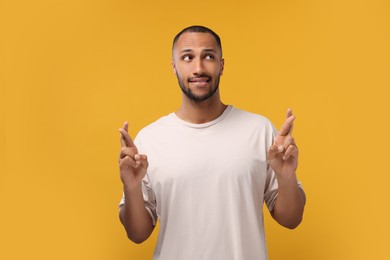 Photo of Young man crossing his fingers on orange background