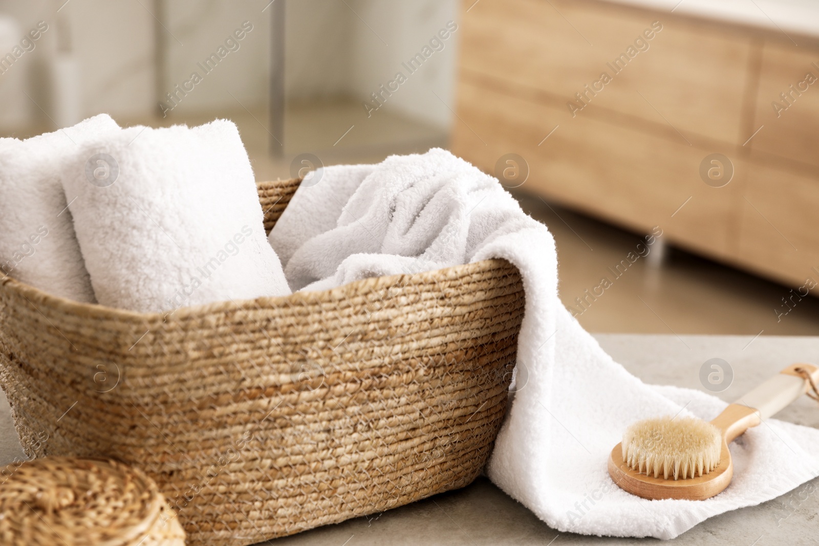 Photo of Wicker basket with clean towels and massage brush on table in bathroom