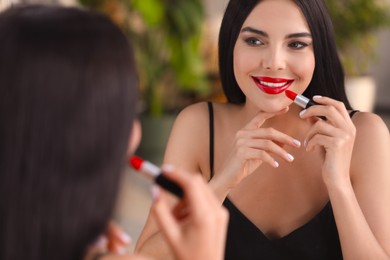 Photo of Young woman applying beautiful red lipstick in front of mirror indoors