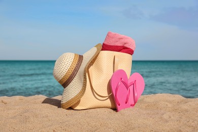 Photo of Summer bag with slippers, beach towel and straw hat on sand near sea