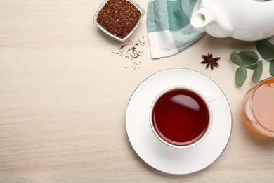 Photo of Freshly brewed rooibos tea, dry leaves, honey and anise on white wooden table, flat lay. Space for text