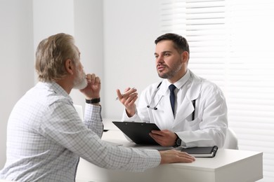 Doctor consulting senior patient at white table in clinic