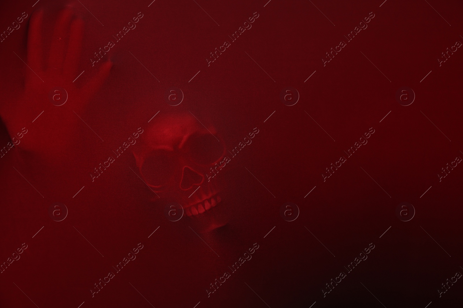 Photo of Silhouette of creepy ghost with skull behind red cloth. Space for text