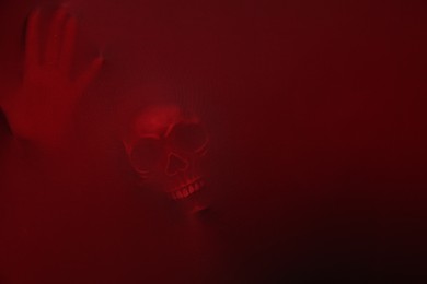 Photo of Silhouette of creepy ghost with skull behind red cloth. Space for text