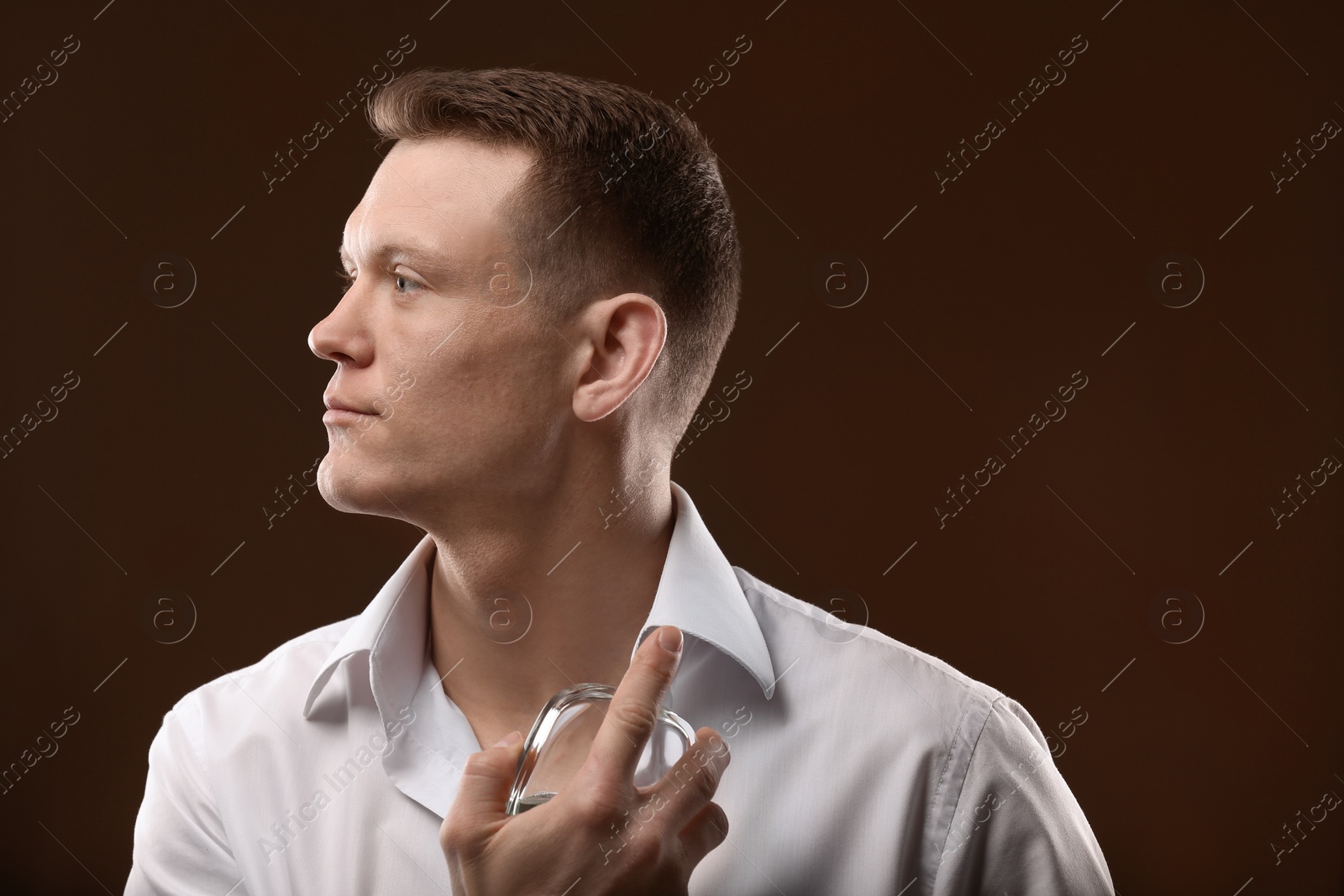 Photo of Handsome man in shirt using perfume on dark background