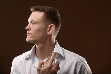 Photo of Handsome man in shirt using perfume on dark background