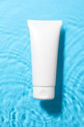 Tube with moisturizing cream in water on light blue background, top view