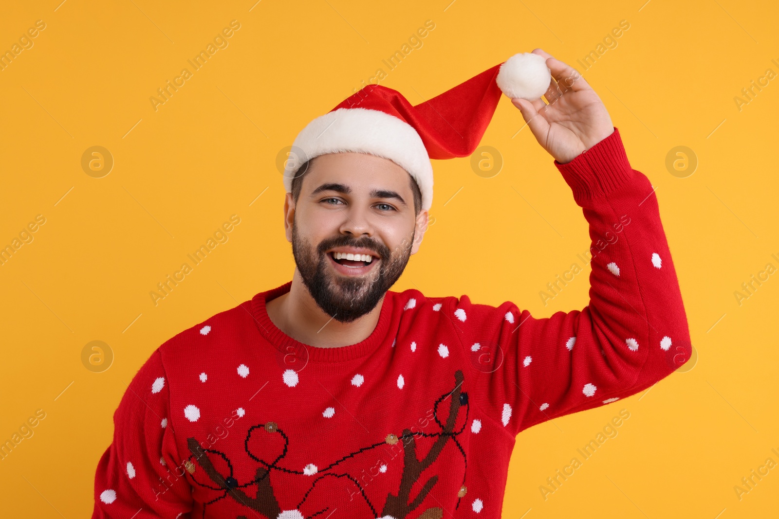 Photo of Happy young man in Christmas sweater and Santa hat on orange background