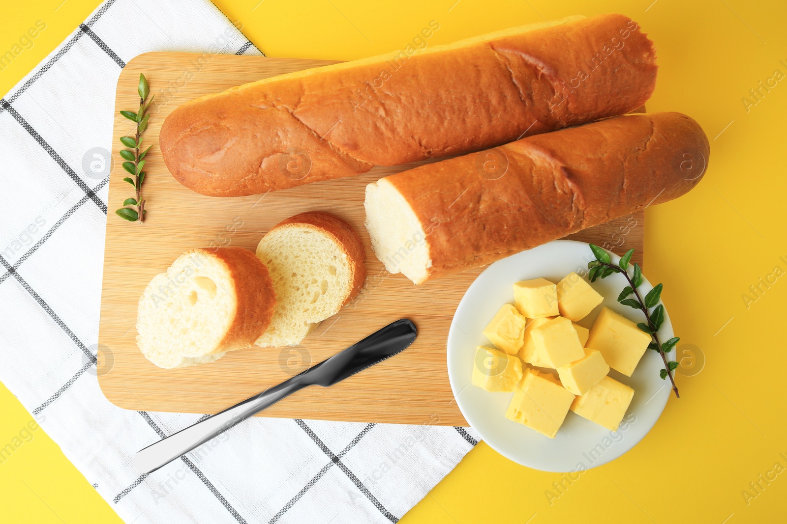 Photo of Whole and cut baguettes with fresh butter on yellow background, flat lay