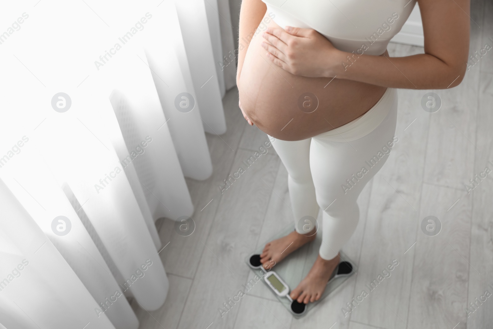 Photo of Pregnant woman standing on scales at home, closeup