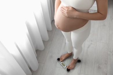 Photo of Pregnant woman standing on scales at home, closeup